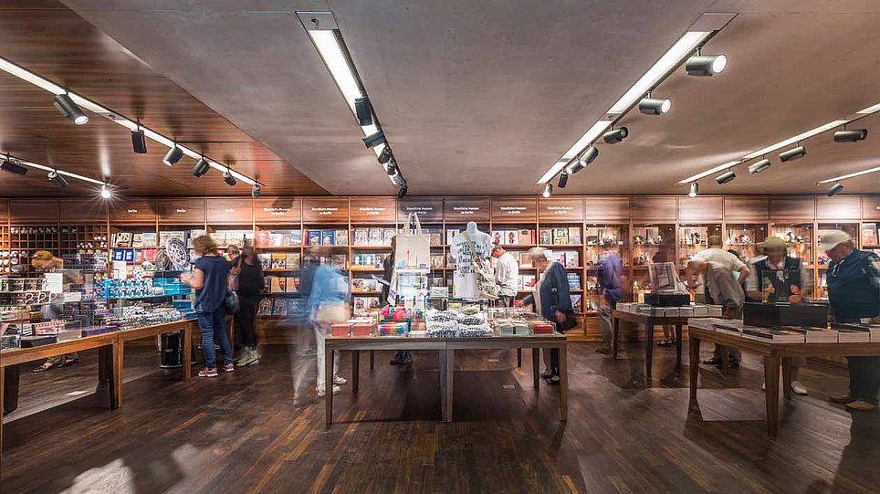 Besucherinnen beim Stöbern im holzverkleideten Museumsshop (öffnet Vergrößerung des Bildes)