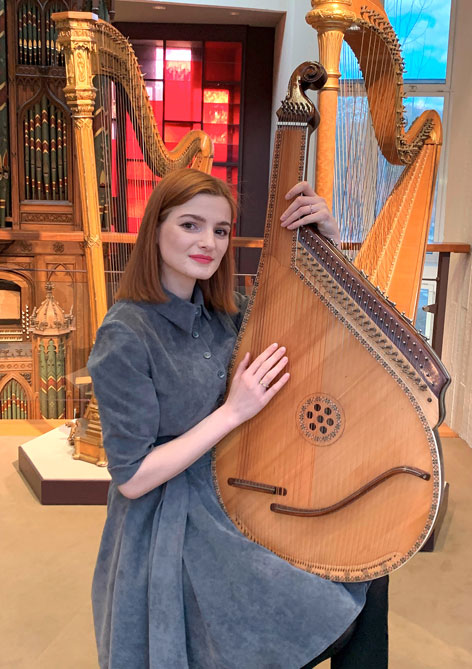 Eine sitzende Frau hält ein großes Saiteninstrument in der Hand