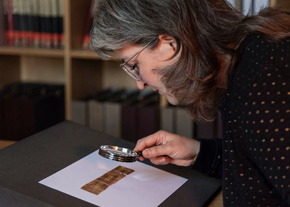 Eine Frau betrachtet mit einer Lupe ein historisches Dokument