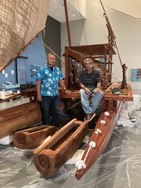 Zwei Männer sitzen auf einem hölzernen Segelboot in einem Museumsraum