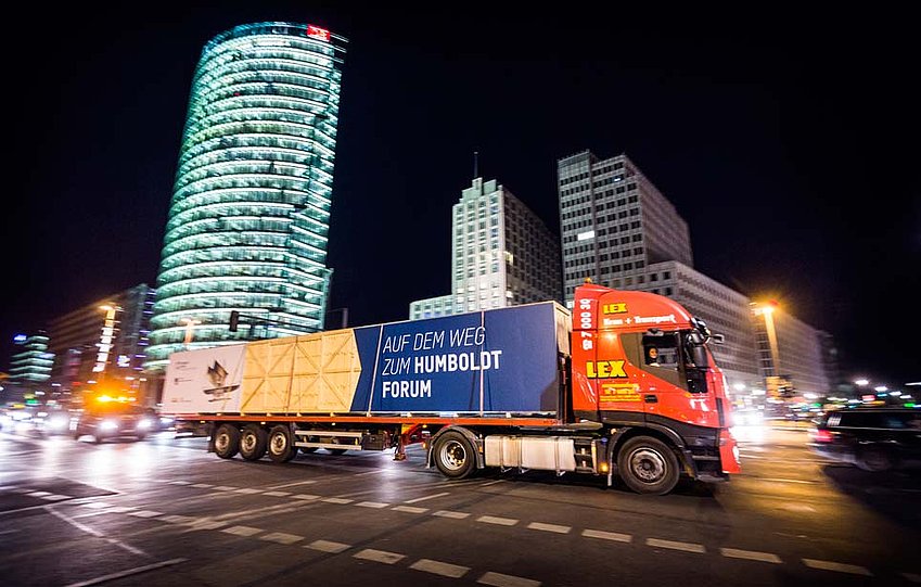 Vor der Kulisse des nächtlichen Berlins fährt ein mit einer großen Kiste beladener LKW eine Straße entlang (öffnet Vergrößerung des Bildes)