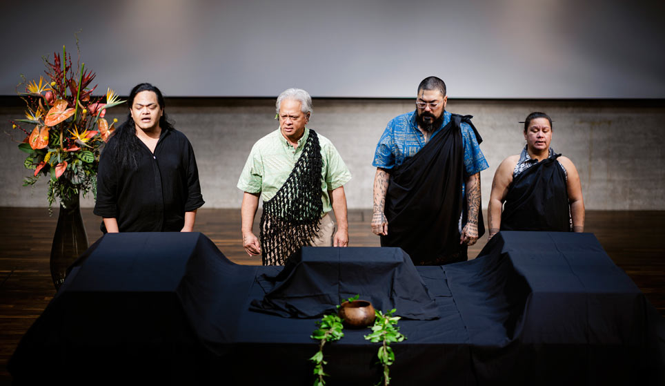 Vier Personen stehen mit geschlossenen Augen vor einem mit schwarzen Tuch bedeckten Tisch