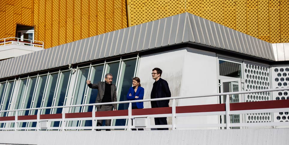 Drei Personen stehen auf der Terrasse eines modernen Gebäudes