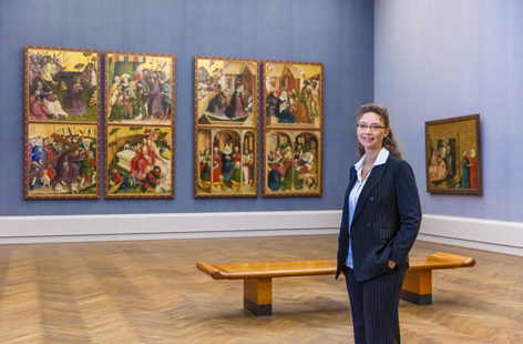 Eine Frau steht in einem Ausstellungsraum mit mittelalterlichen Gemälden