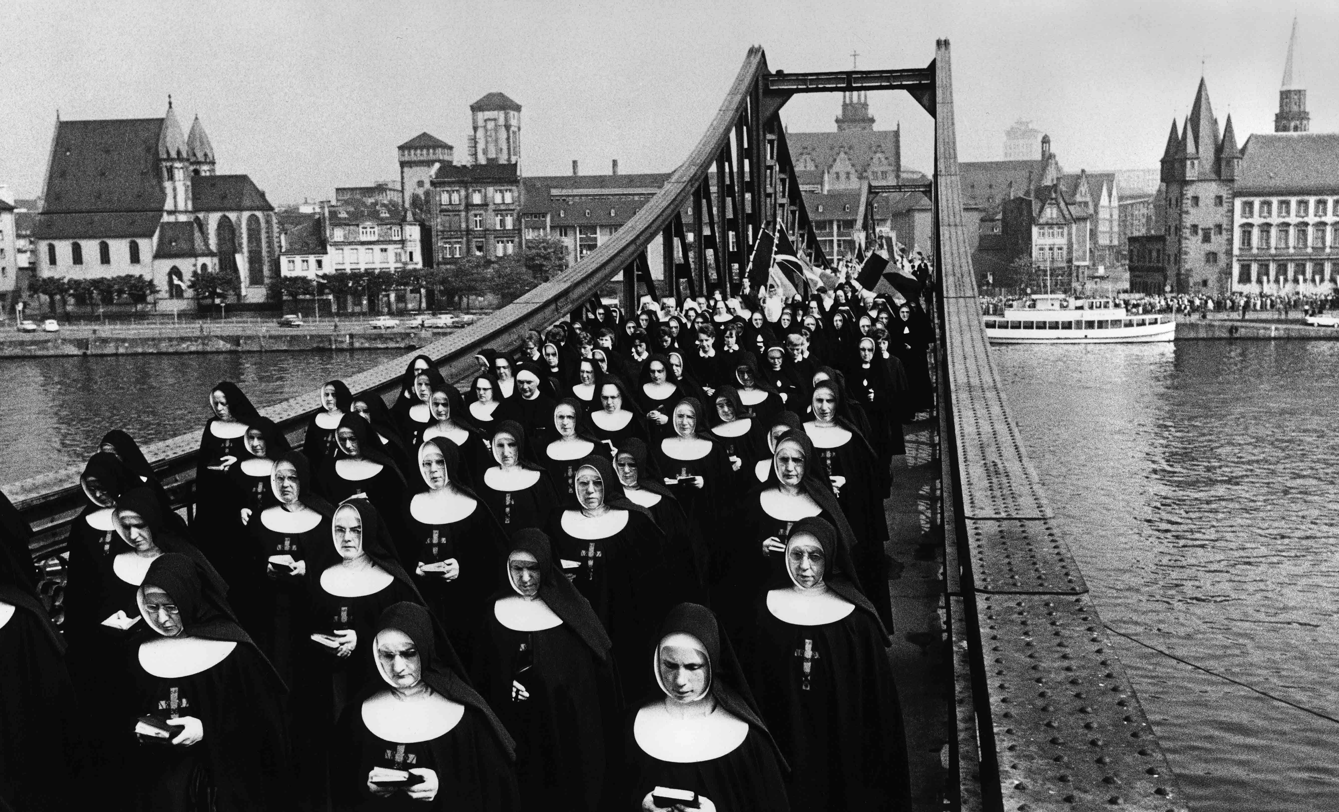 Schwarz-weiß Fotografie, die eine Gruppe lesender Nonnen auf einer Brücke zeigt.
