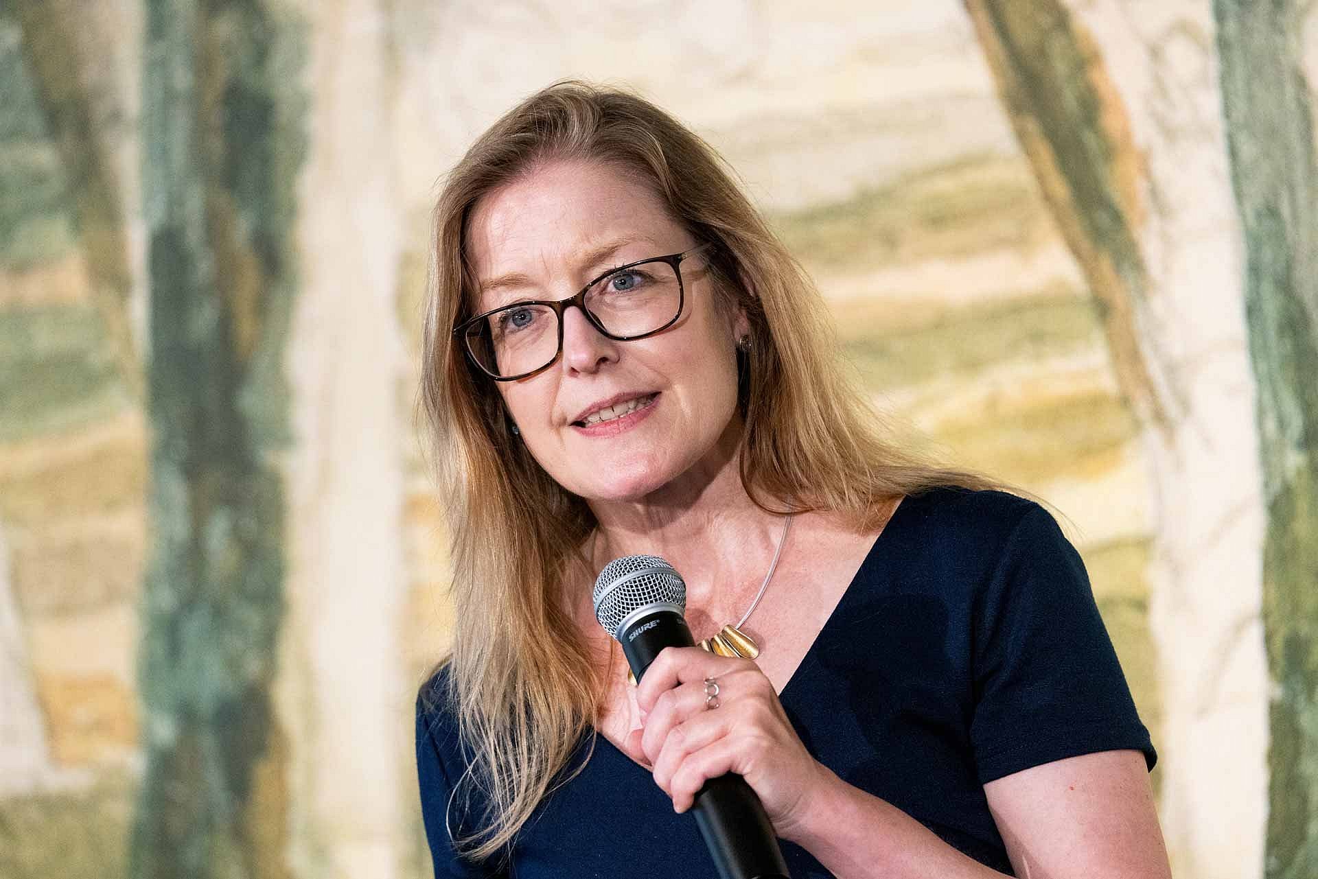 Eine blonde Frau mit Brille spricht in ein Mikrofon