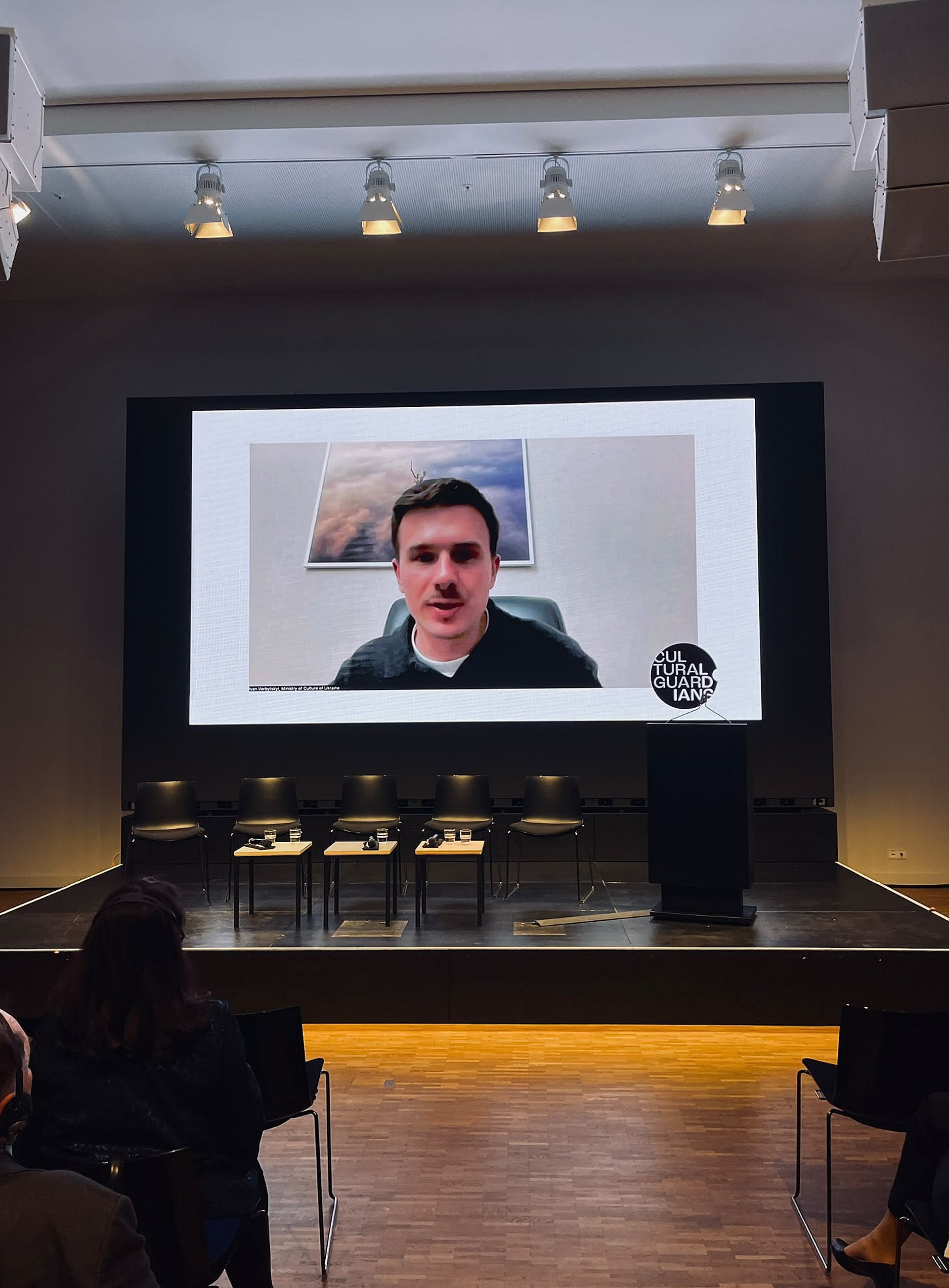 Mann in einem Videocall, groß auf die Leinwand eines Veranstaltungssaals projiziert