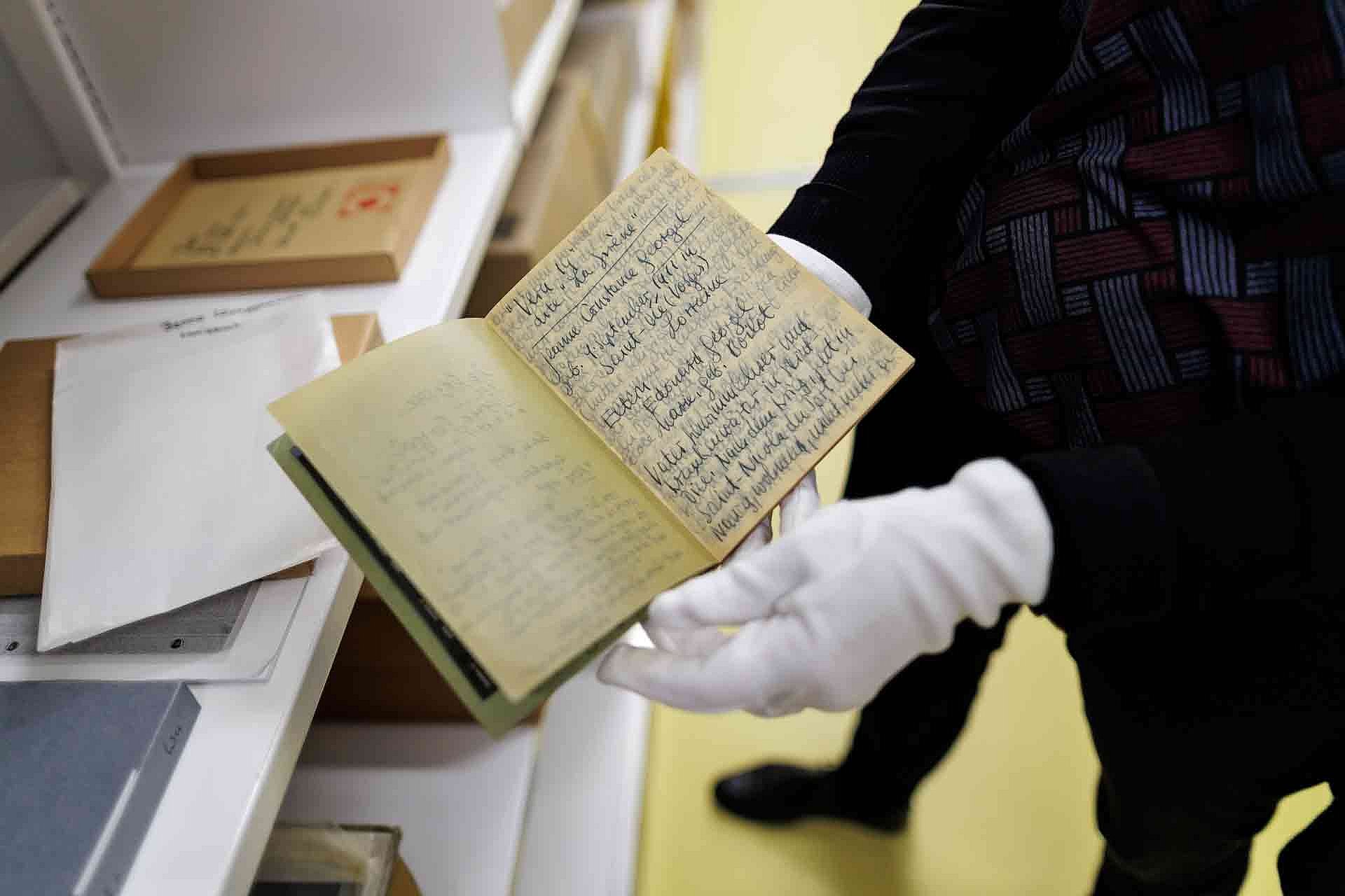 Eine Person mit weißen Handschuhen zeigt ein handgeschriebenes Buch