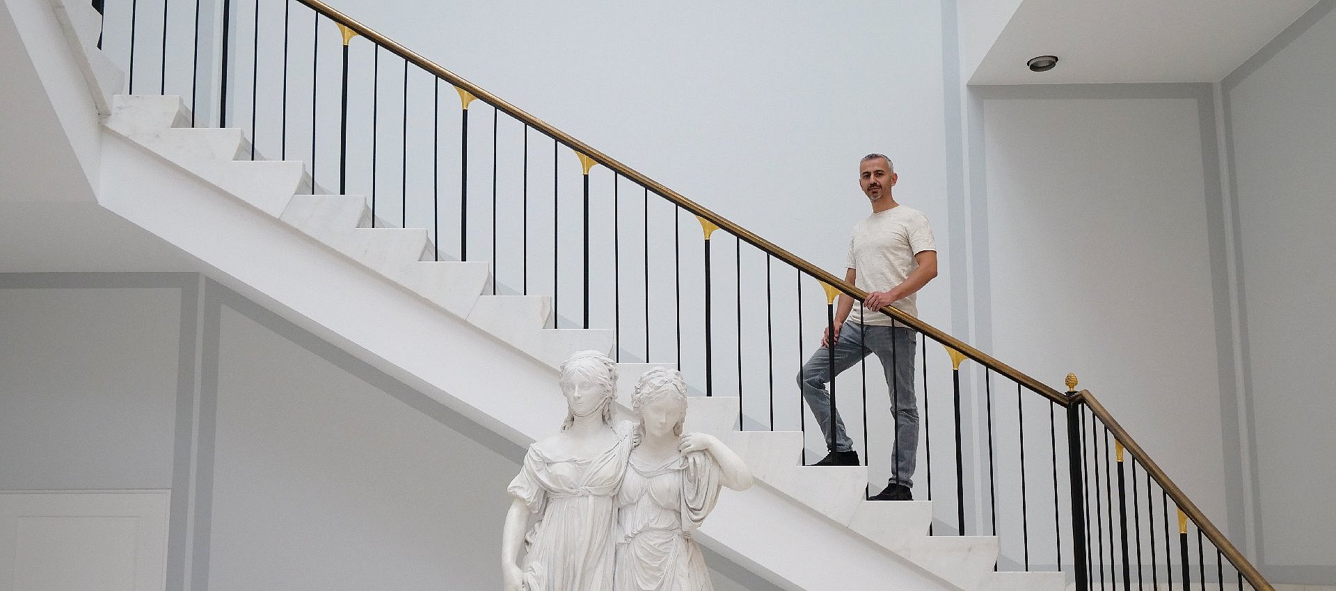Mann steht auf Treppe, vor ihm Skulptur