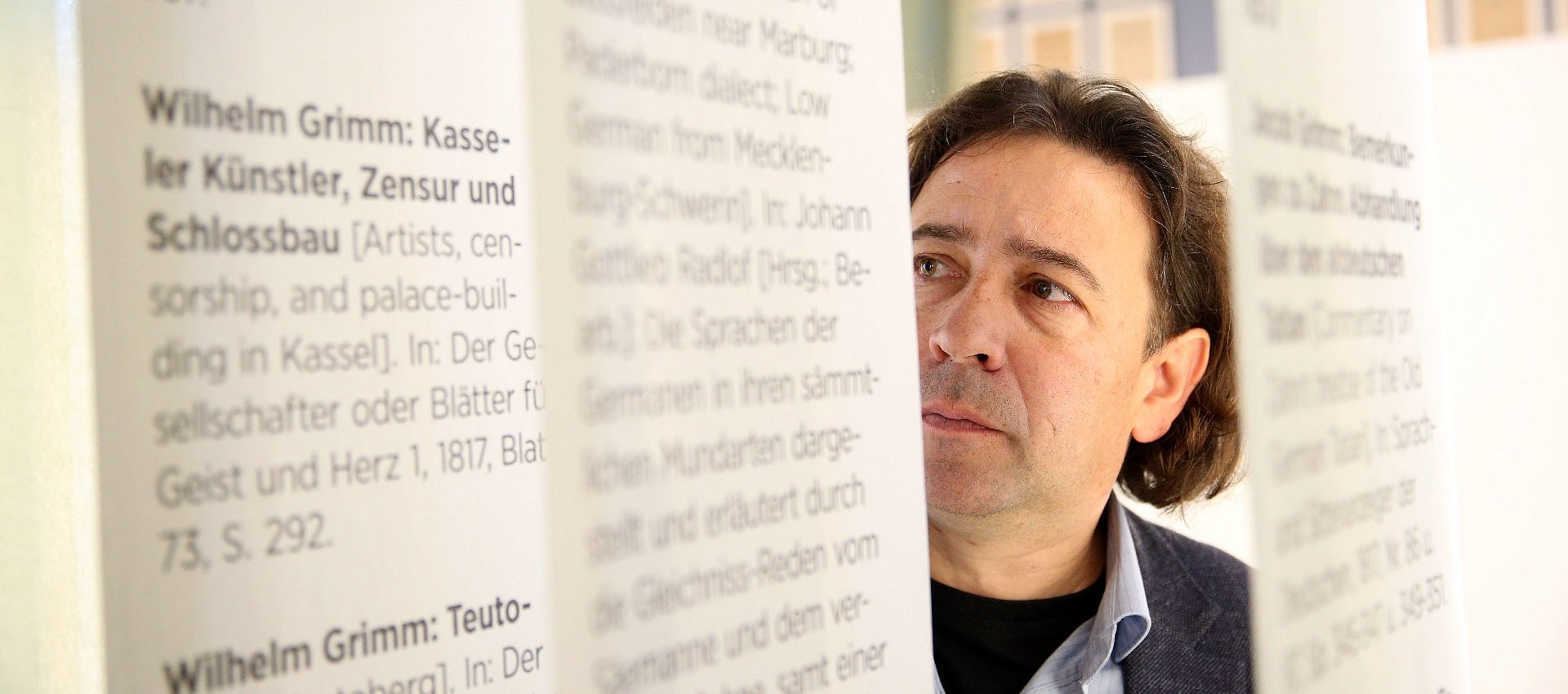 Portrait eines Mannes der durch runterhängende Textbögen guckt