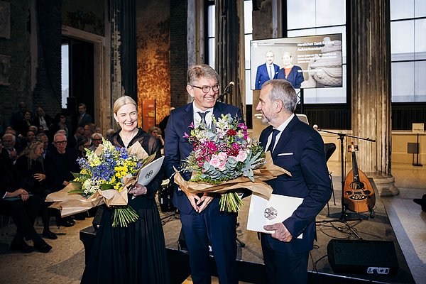 drei Menschen mit zwei Blumensträußen