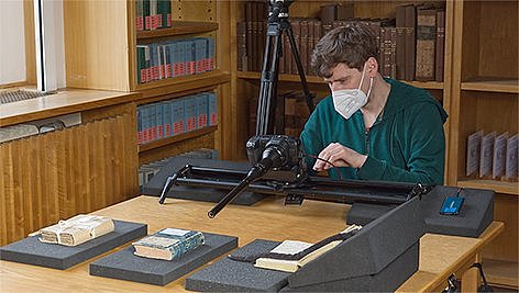 Eine Person betrachtet Fotos an einem Tisch durch ein Objektiv.