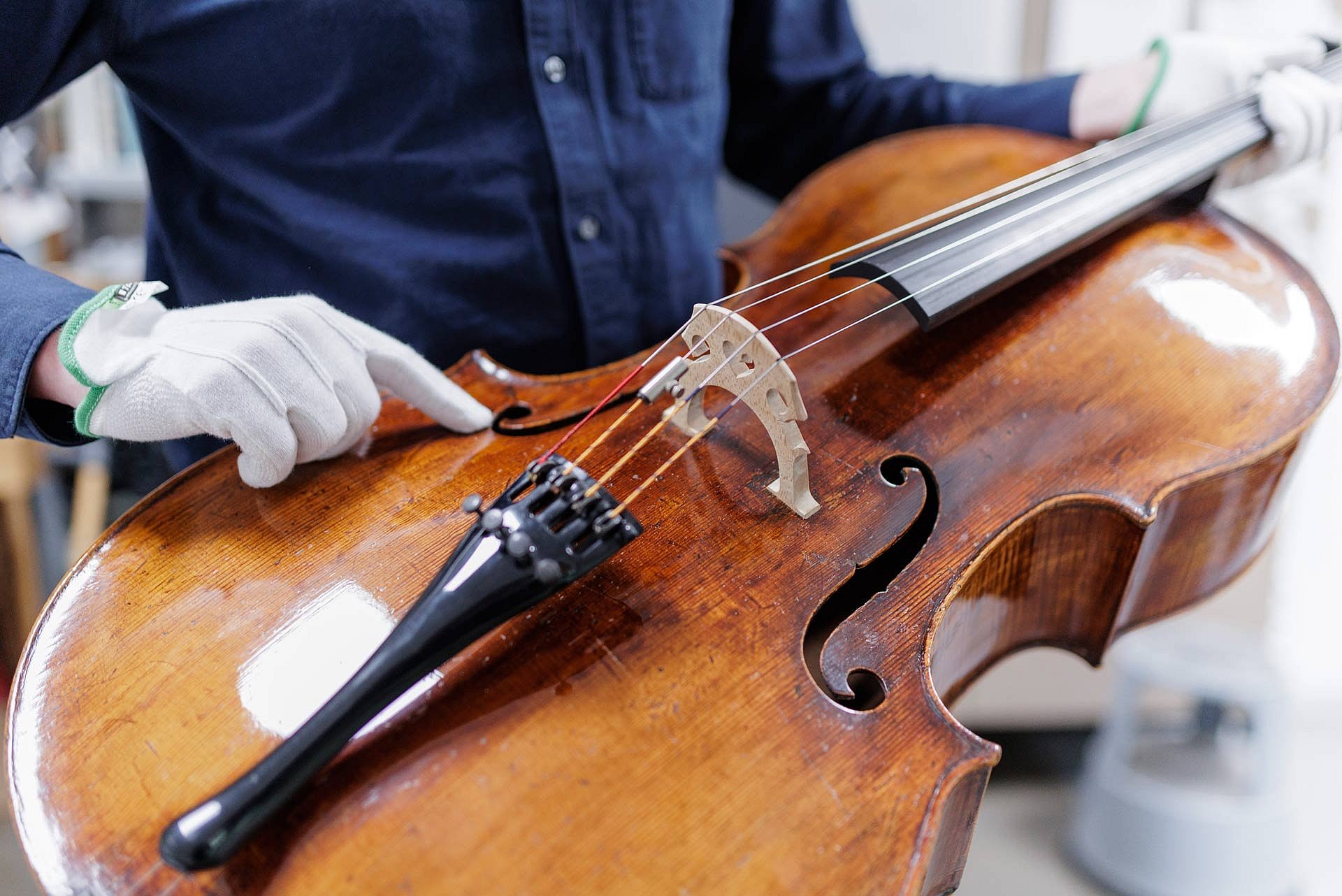 Eine Hand im weißen Handschuh zeigt auf eine Stelle auf einem Cello