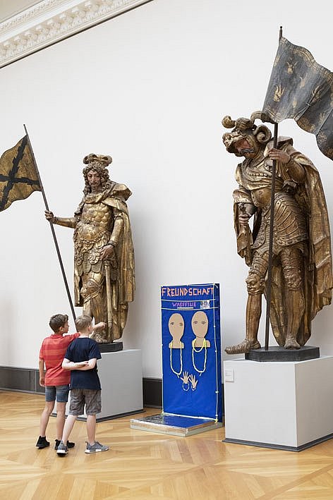 Zwei Schüler stehen im Museum vor zwei überdimensionierten Ritterstatuen