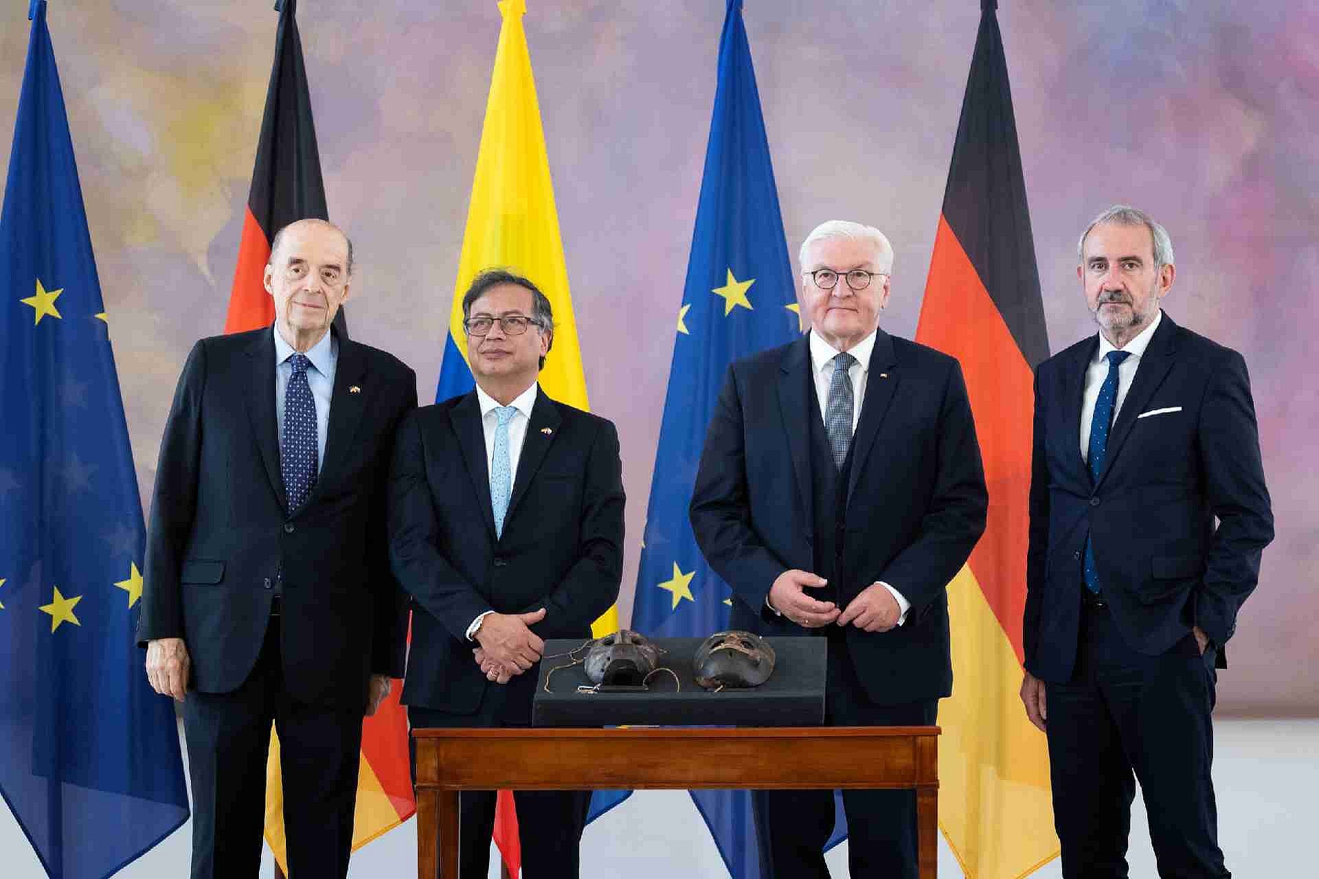 vier Männer vor EU-, deutscher und kolumbianischer Flagge mit Masken im Vordergrund