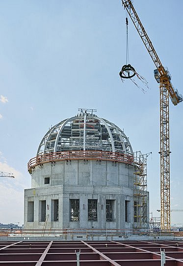 Blick auf eine sich im Bau befindlichen Gebäudekuppel, über der ein grüner Kranz an einem Kran schwebt (öffnet Vergrößerung des Bildes)