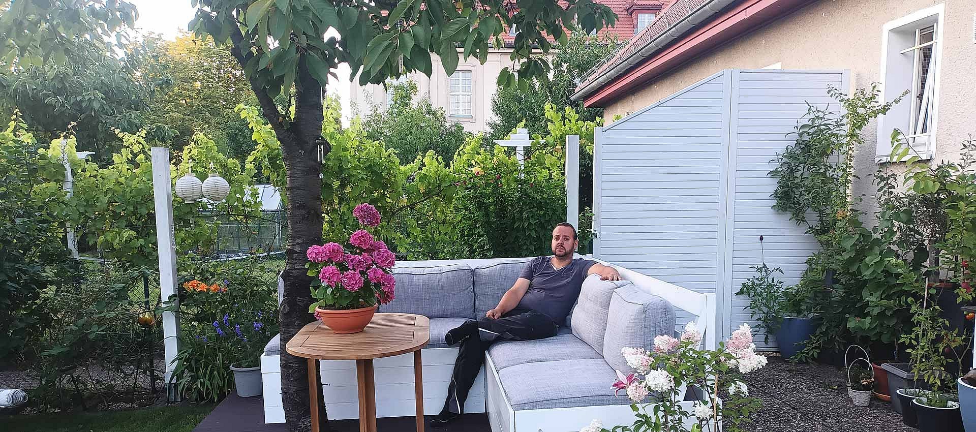 Mann sitzt auf seiner Terrasse im Grünen