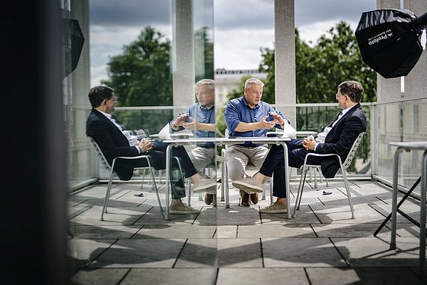 Matthias Wemhoff sitzt in einem Caféstuhl und spricht mit einem Mann im Anzug