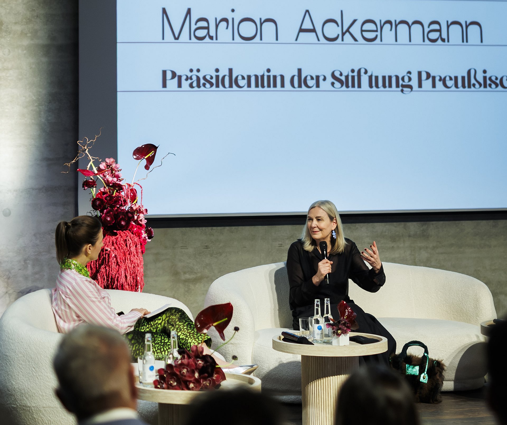 Marion Ackermann spricht beim Jahresempfang der Stiftung Preußischer Kulturbesitz vor Publikum auf einer Bühne; hinter ihr ist ihr Name auf einer Projektionsfläche zu sehen.