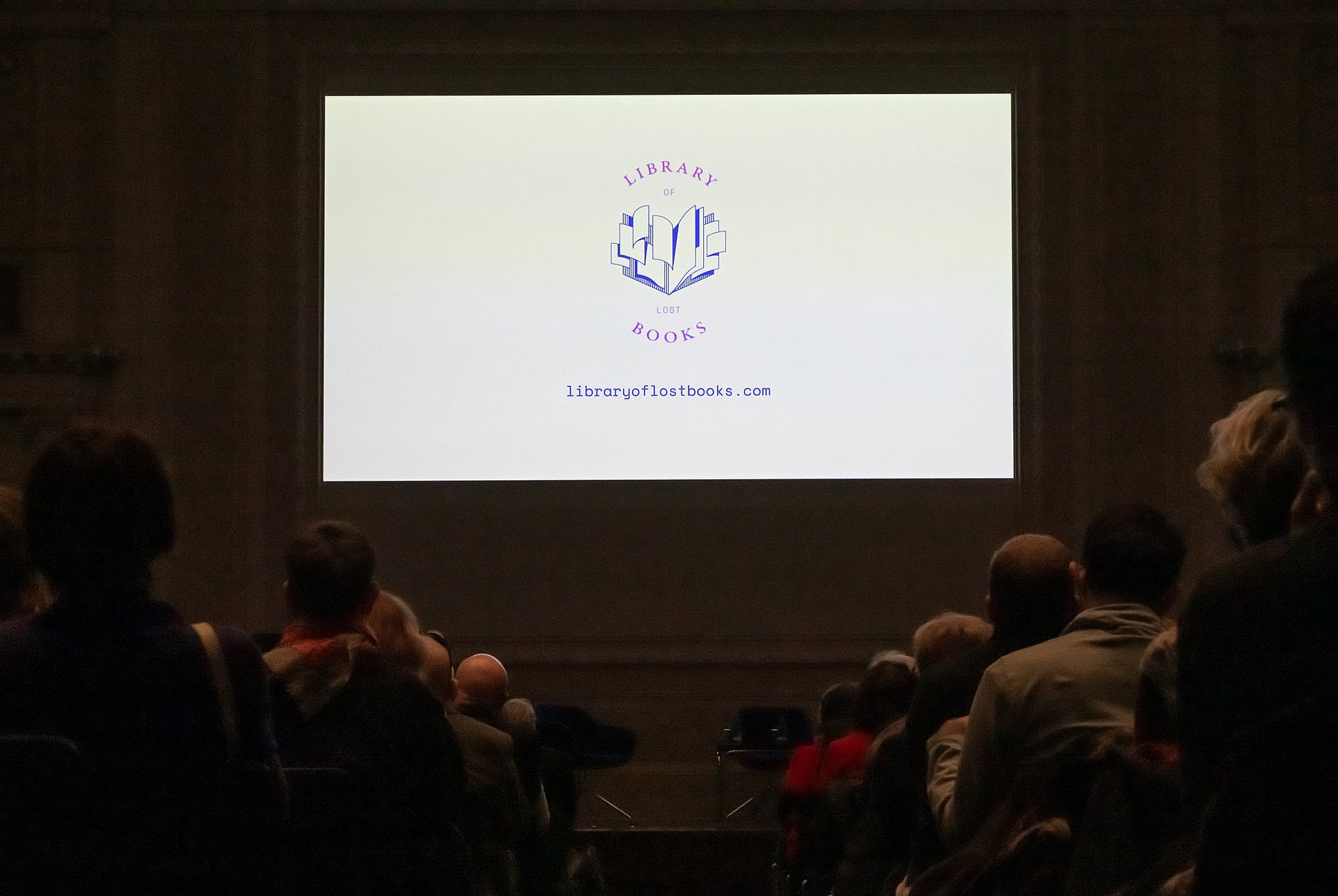 Große Leinwand vor Publikum, darauf Text: The Library of Lost Books