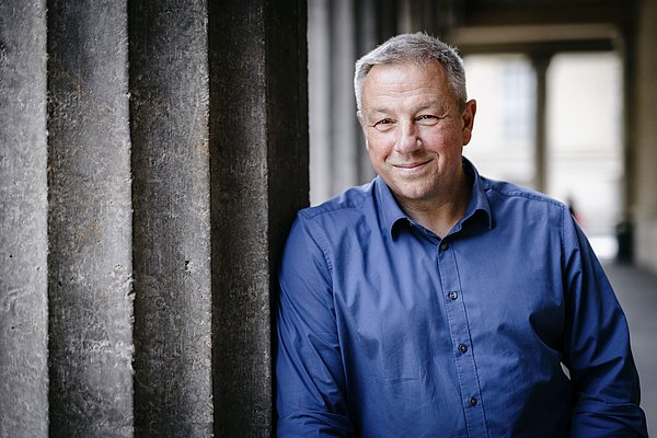 Der Museumsdirektor Matthias Wemhoff lehnt in einem blauen Hemd an einer Steinsäule der Kolonnaden.