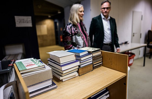 Zwei Menschen stehen in einer Bibliothek hinter Bücherstapeln