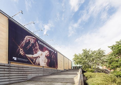 Ein großes Plakat hängt an einem Gebäude, zu dem eine Treppe hinaufführt