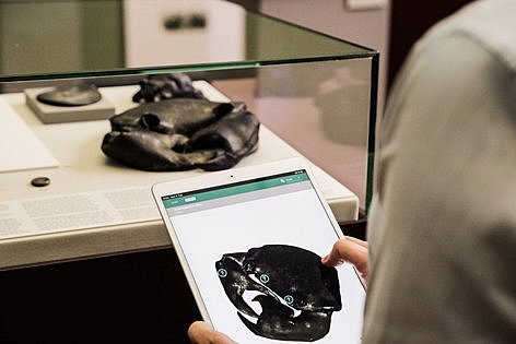 Eine Person hält ein Tablet in der Hand und steht vor einer flachen Glasvitrine