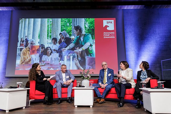 JE25 Personen auf rotem Sofa auf Bühne