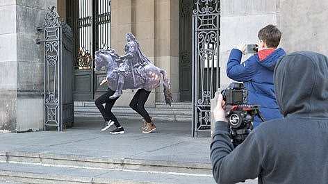 Pappferd mit menschlichen Beinen trabt aus Museum, fotografiert von zwei MEnschen 