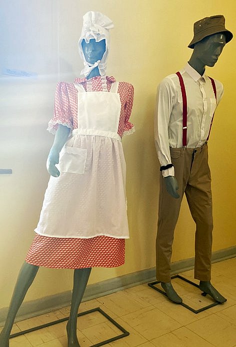 Schaufensterpuppen, jeweils bekleidet mit knielangem Kleid und Schürze, bzw. Hemd, Hose und Hosenträgern