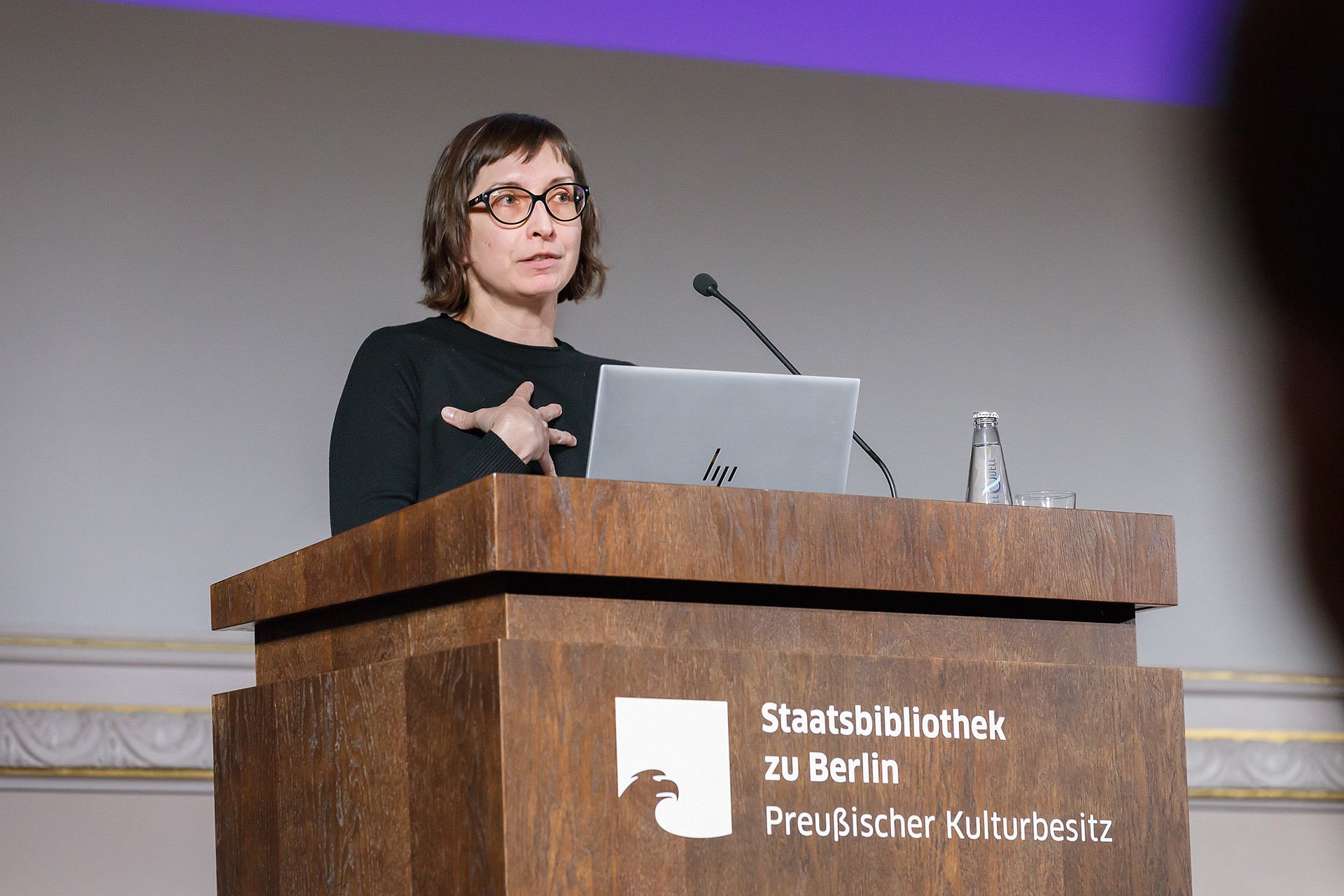 Frau mit Brille spricht an einem Rednerpult auf einer Bühne