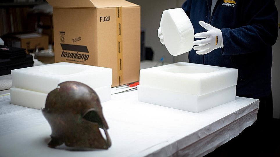 Tisch mit einem Metallhelm, einem Pappkarton und verschiedenen Schaumstoffteilen in unterschiedlichen Größen (öffnet Vergrößerung des Bildes)