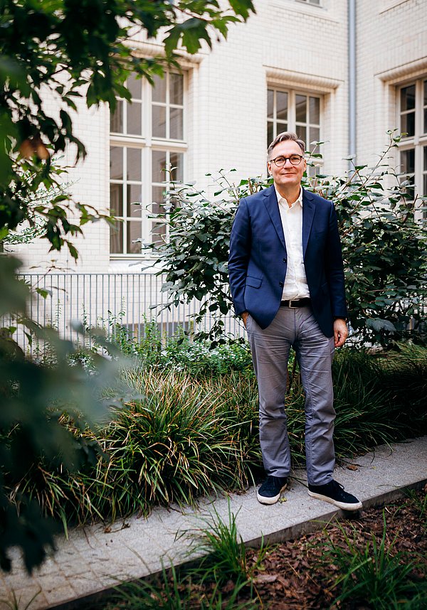 "vertrauen, öffnen, beteiligen" lautet die Devise der Stabi unter Generaldirektor Achim Bonte Ein Mann im blauen Sakko steht in einem begrünten Hinterhof
