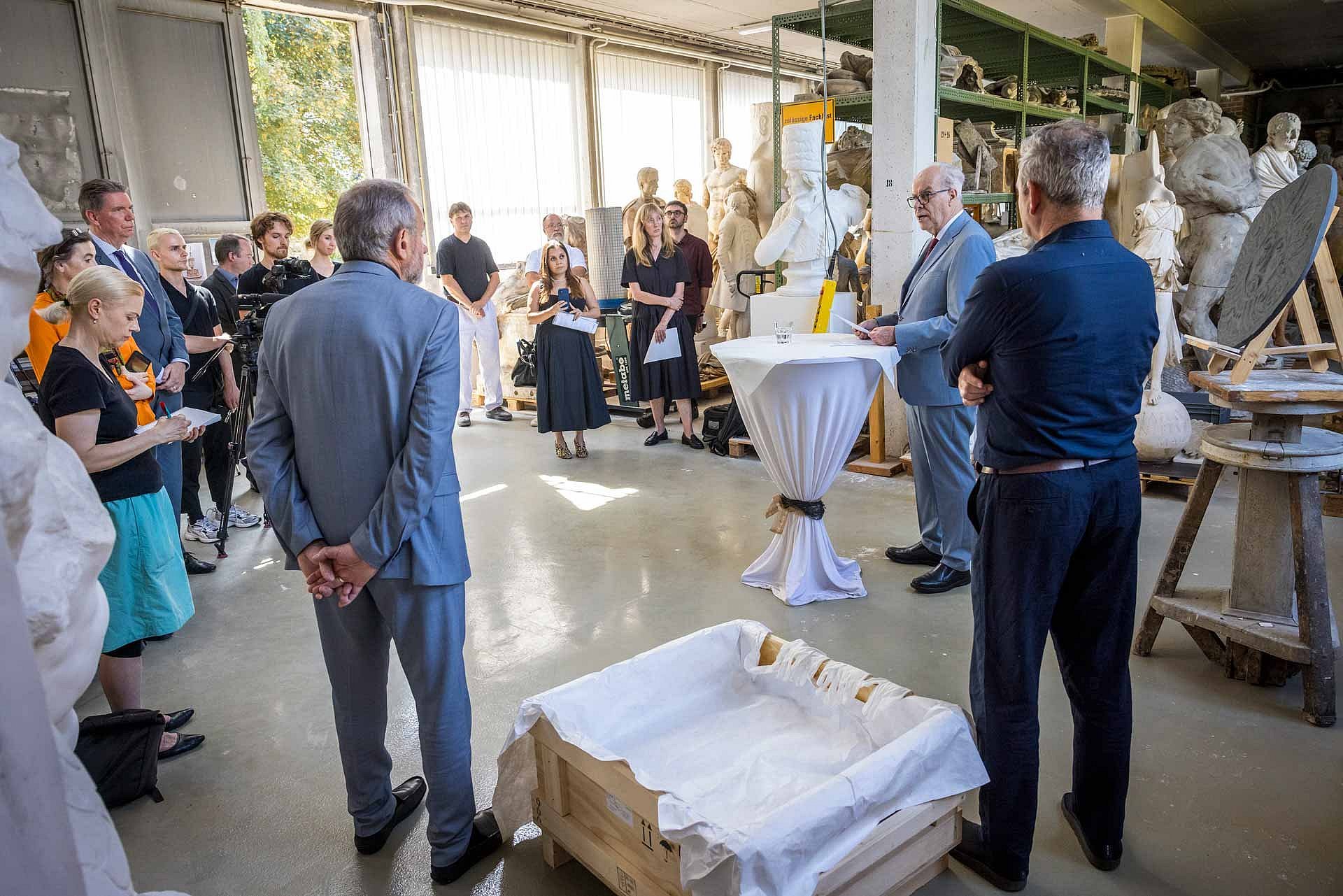 Menschen stehen im Halbkreis um einen sprechenden Mann