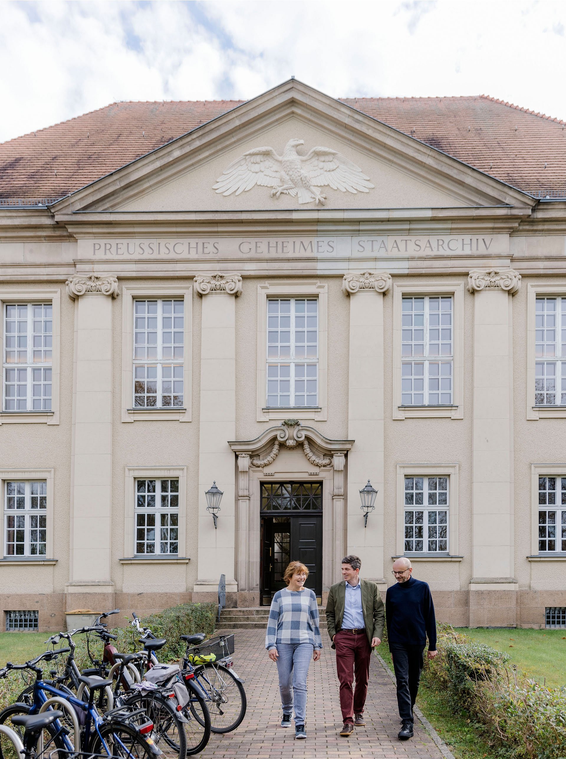 Drei Menschen verlassen ein altehrwürdiges Gebäude 