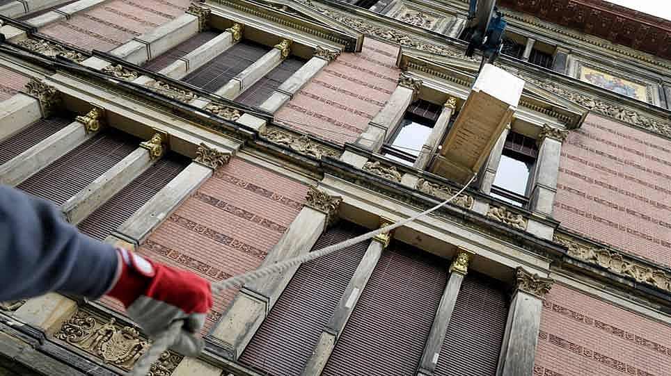 Blick von unten auf eine Holzkiste, die von einem Kran durch ein Fenster nach draußen gezogen wird (öffnet Vergrößerung des Bildes)