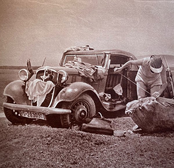 Sepiaaufnahme eines Autos auf freiem Feld, daneben eine Person