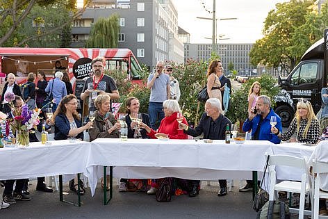 Menschen prosten sich an einer Tafel im Freien gutgelaunt zu (öffnet Vergrößerung des Bildes)