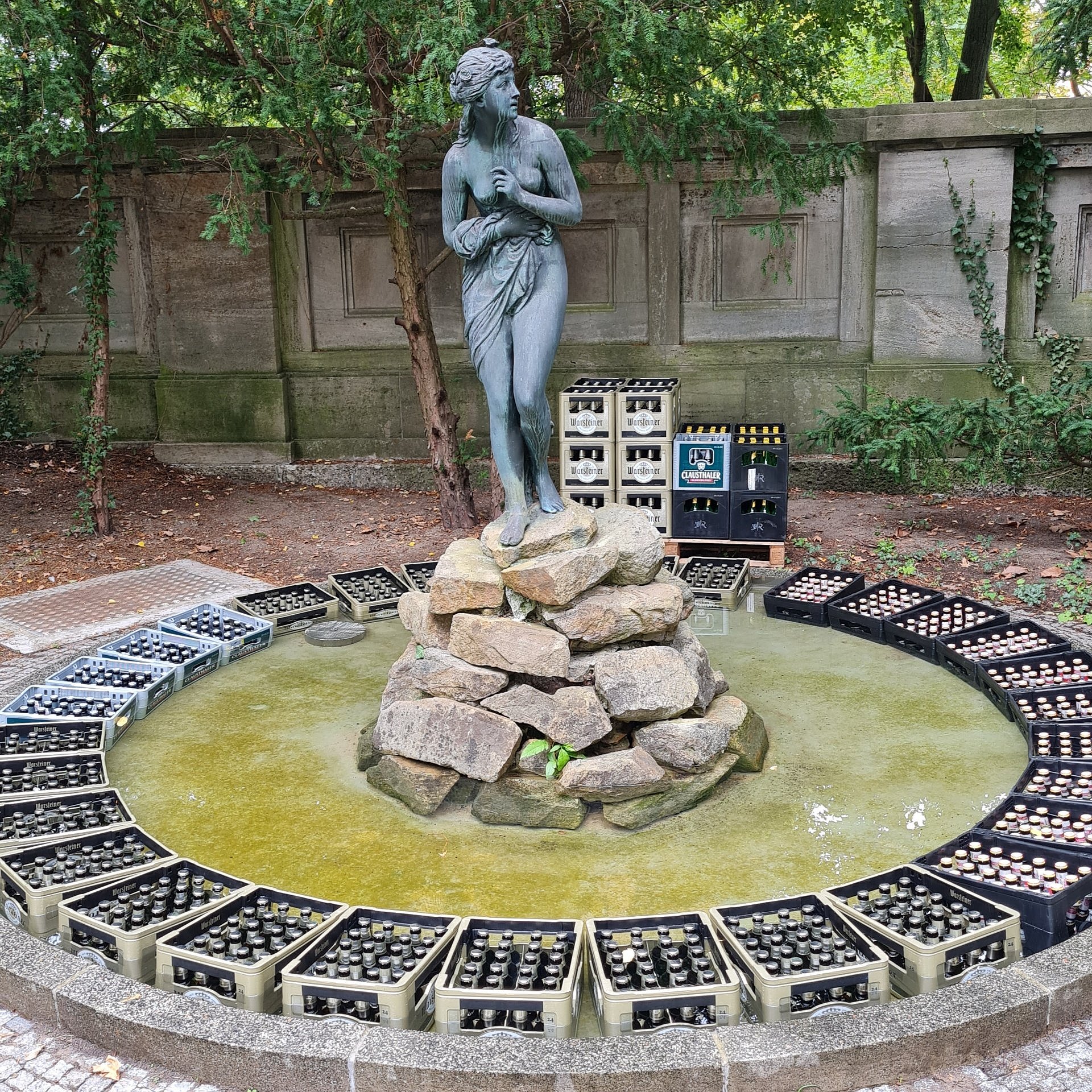 ein Brunnen mit einer Frauenstatue in der Mitte und Bierkästen drumherum