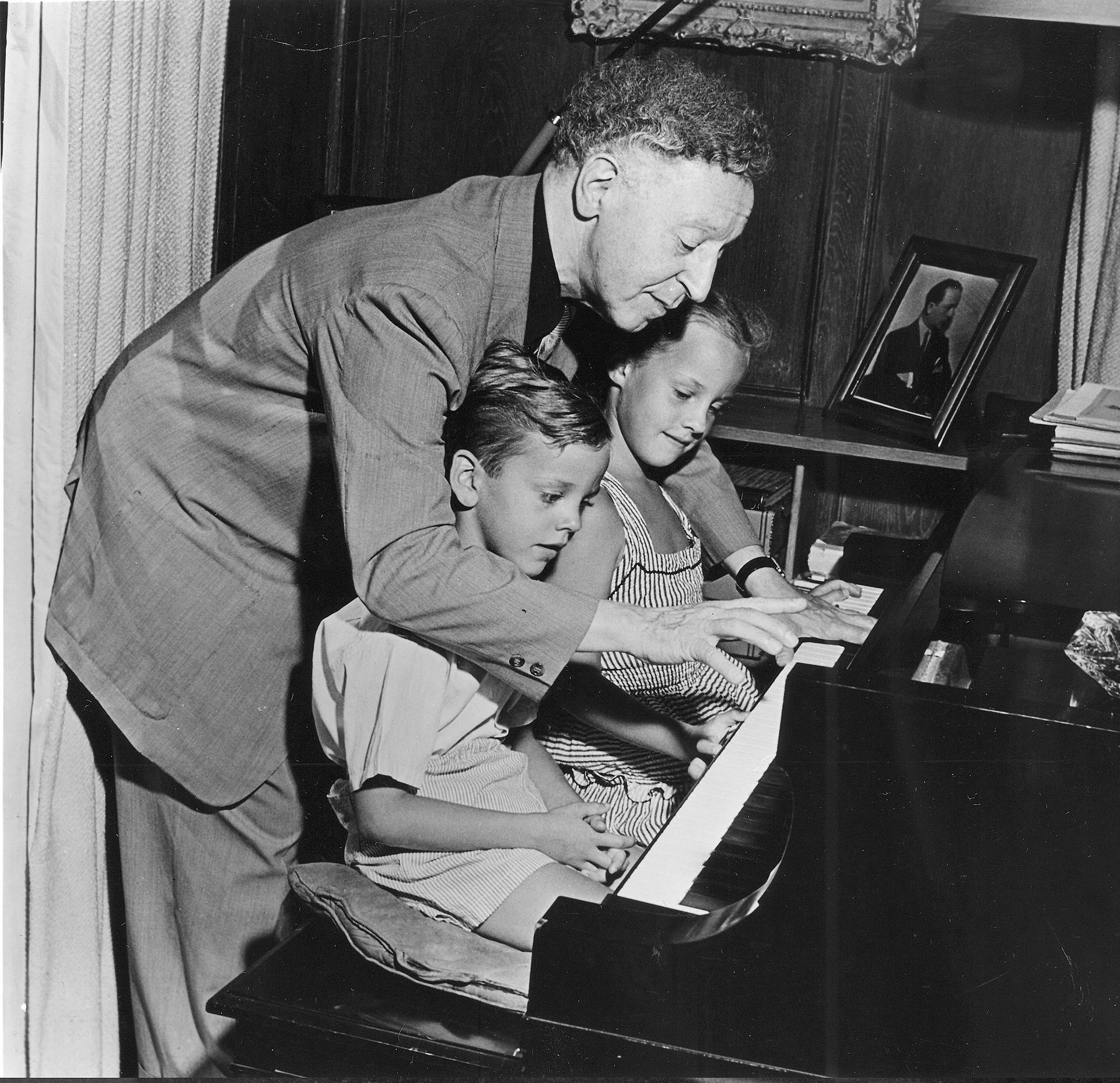 Historisches Bild eines Mannes, der sich mit zwei Kindern über die Tastatur eines Klaviers beugt