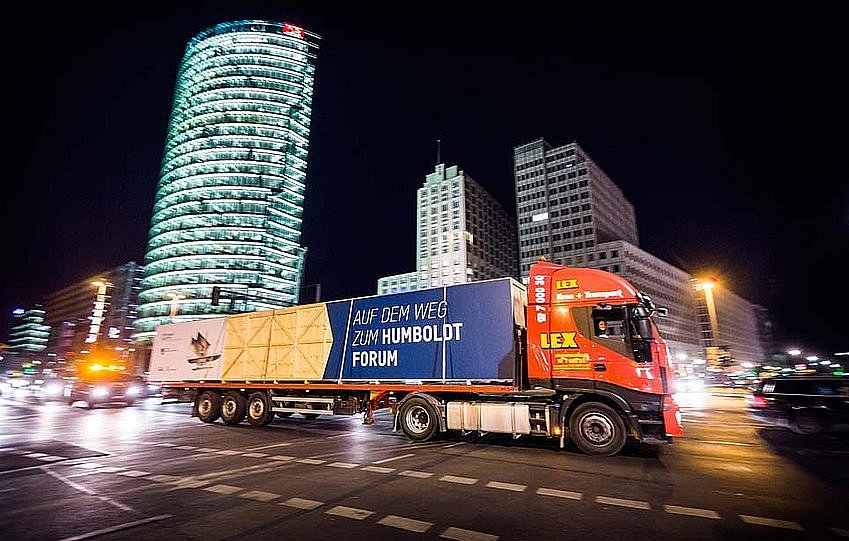 Vor der Kulisse des nächtlichen Berlins fährt ein mit einer großen Kiste beladener LKW eine Straße entlang (öffnet Vergrößerung des Bildes)