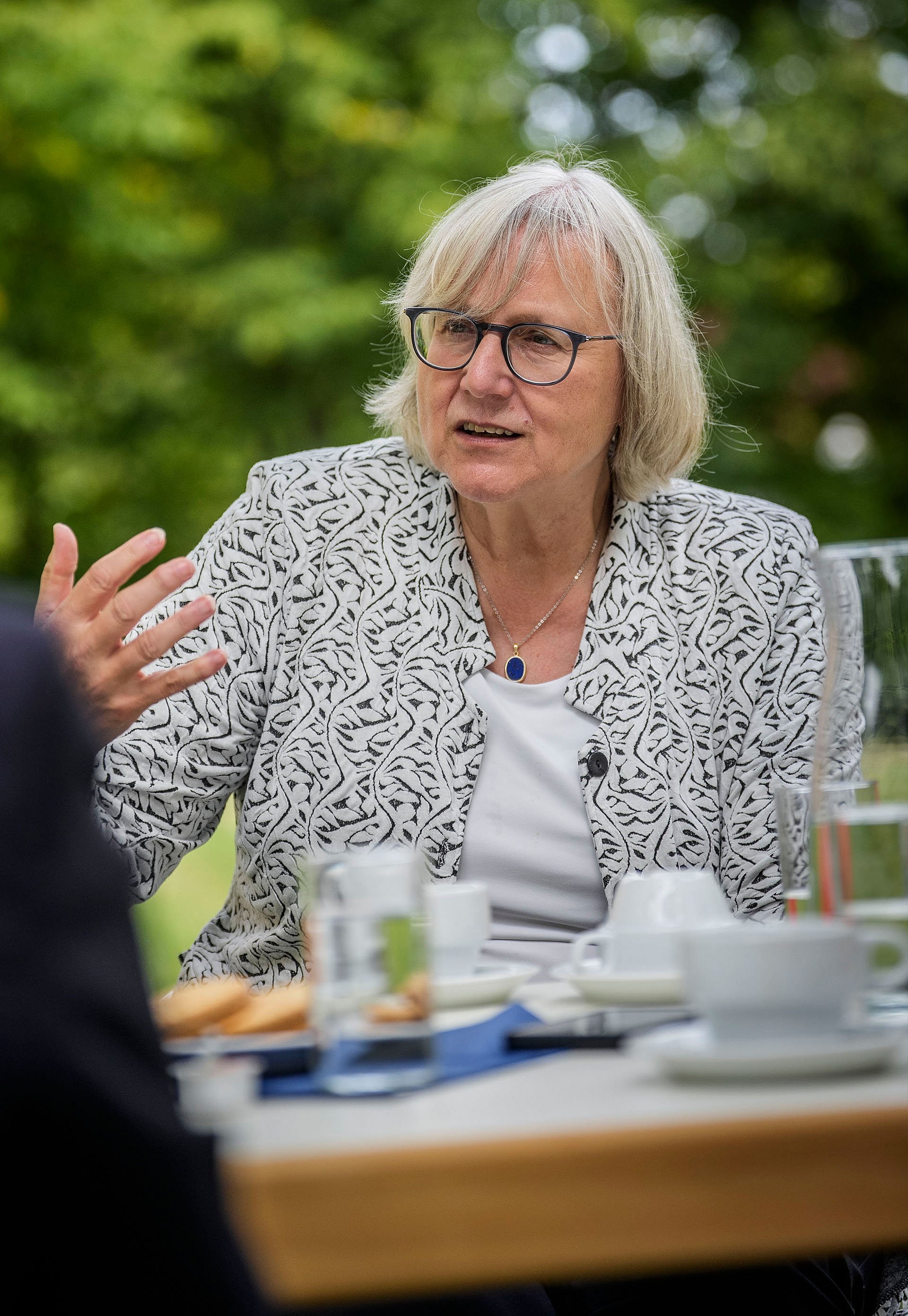 Frau sitzt am Tisch und redet gestikulierend