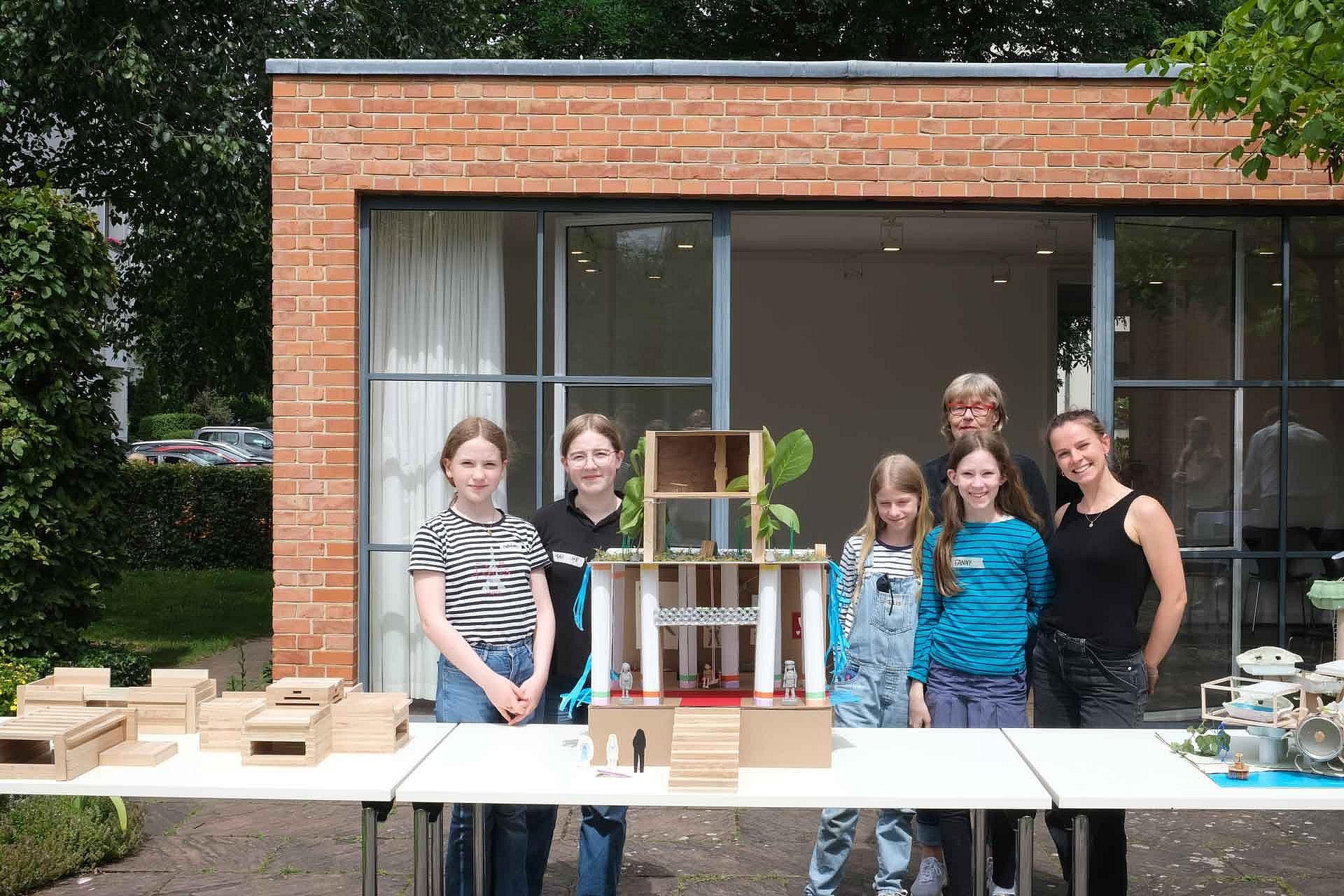 Kinder und eine Frau präsentieren ein Architekturmodell auf einem Tisch
