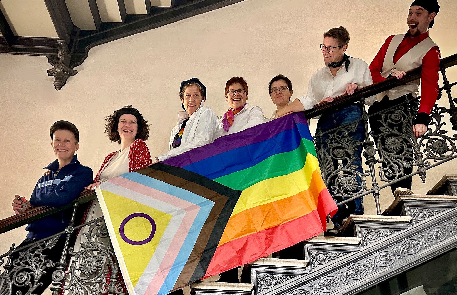 Eine Gruppe Menschen auf einer Treppe vor einer Regenbogenfahne