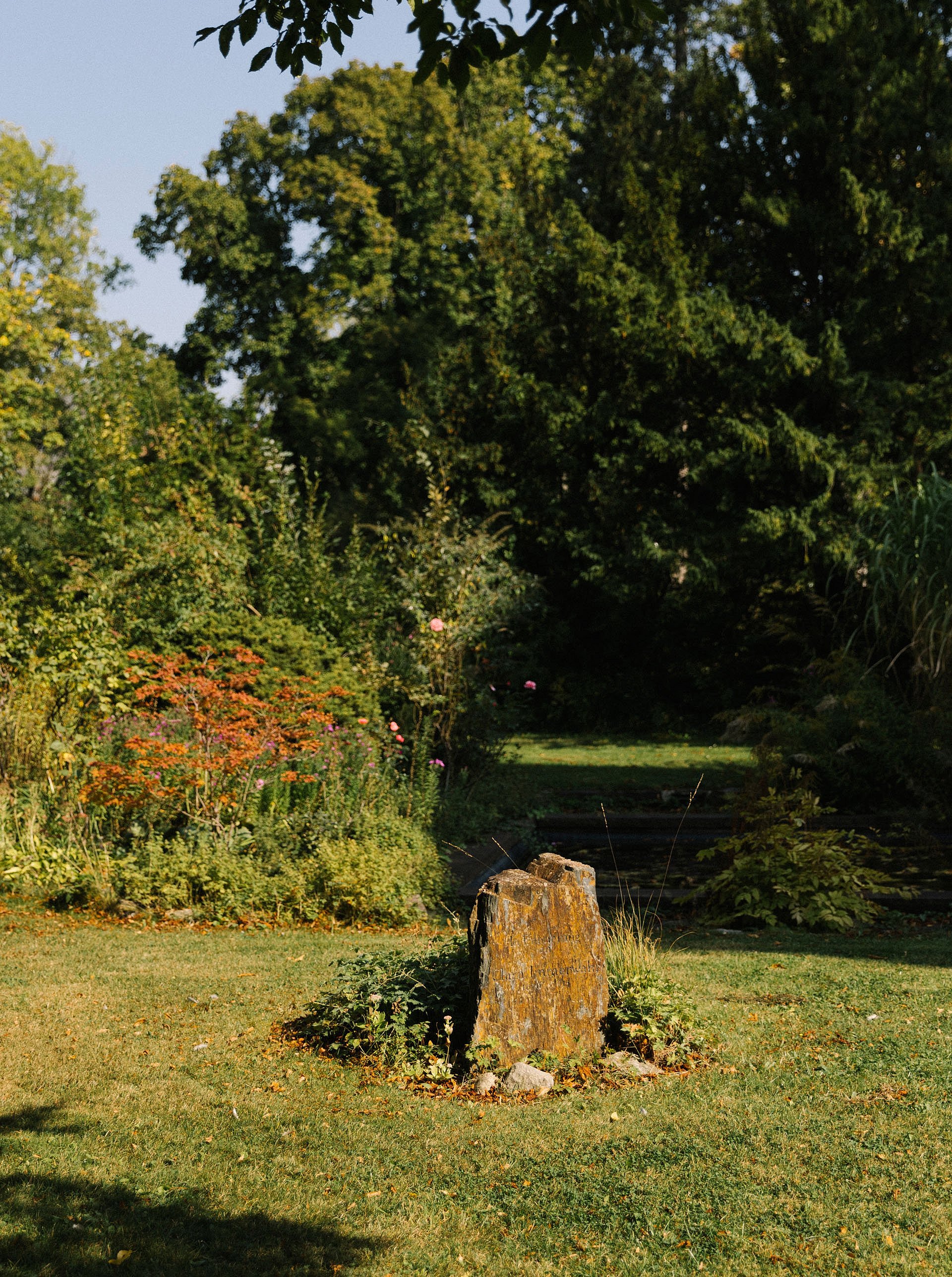 Bemooster Gedenkstein in einem von Herbstsonne durchflutetem Garten