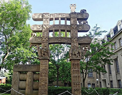 Asiatisches Steintor vor einem Gebäude, daneben Bäume