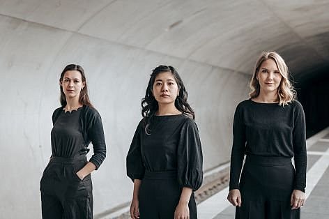 Die drei Musikerinnen von Trio Hannari stehen mit ihren Instrumenten und schwarzer Kleidung vor einer Betonwand