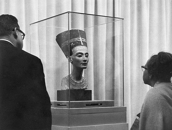Besucher*innen betrachten die Büste der Nofretete Historisches schwarz-weiß Foto zweier Menschen vor einer ägyptischen Büste in einer Glasvitrine
