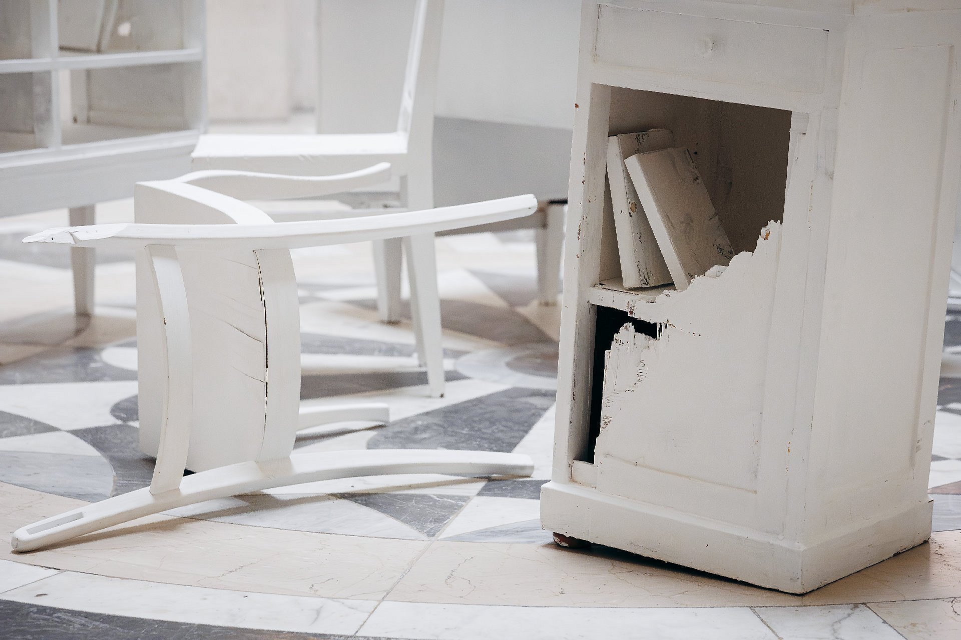 umgekippter weißer Stuhl neben kaputtem Schrank